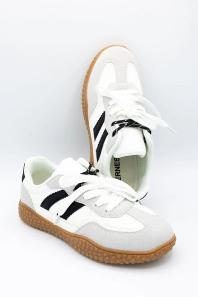 A pair of white sneakers with black detailing on a basic studio background