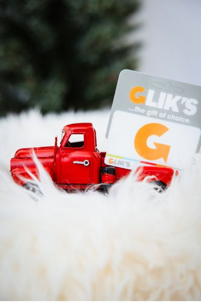 Red toy truck next to a Glik's gift card on a white surface with blurred greenery in the background
