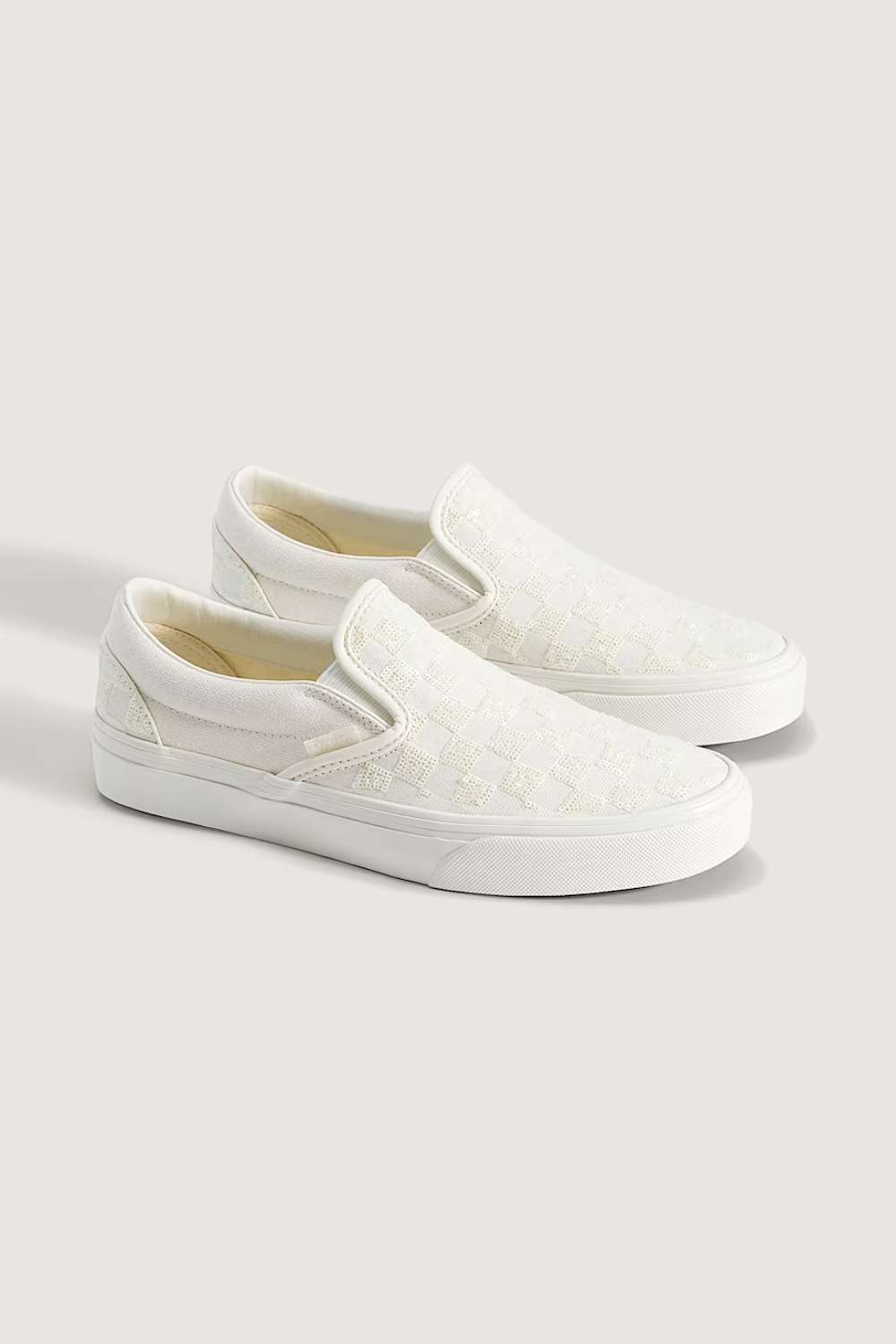 A pair of white slip-on platform sneakers with a subtle embossed pattern, displayed on a light beige background.