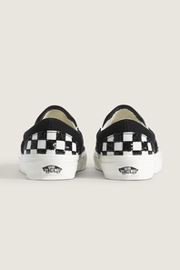 A pair of Vans slip-on sneakers shown from the back, featuring a black and white checkerboard pattern on the sides and white rubber soles with the Vans logo.