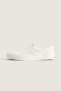 A single white slip-on platform sneaker with a subtle embossed pattern on the upper, shown in profile against a solid light beige background.
