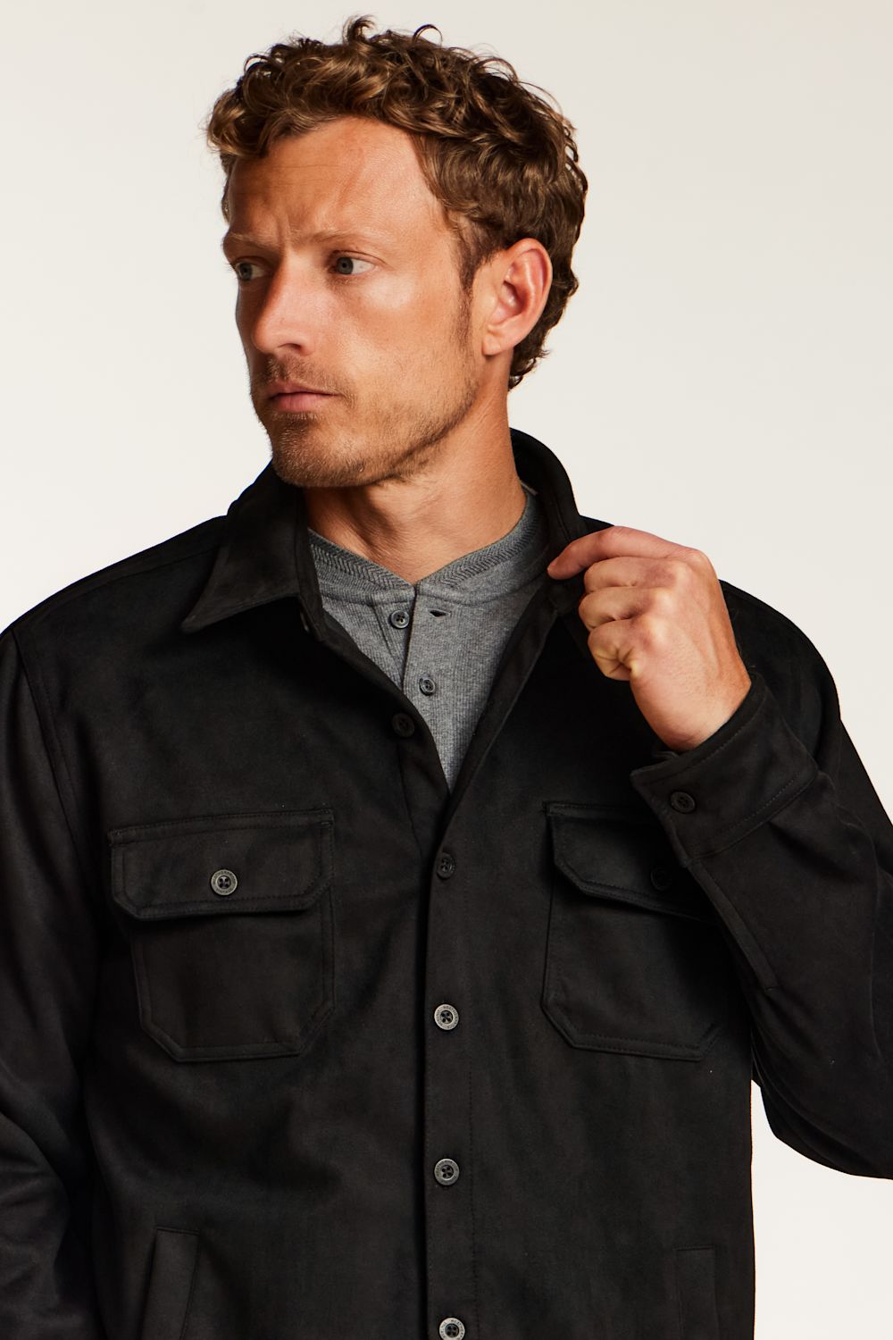 A man wearing a black overshirt over a gray henley shirt, photographed against a plain light background.