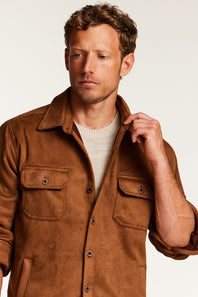 A man wearing a brown suede-like button-up shirt jacket over a light beige knit sweater, photographed against a plain light background.