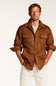 A man wearing a brown suede-like button-up shirt jacket over a beige knit sweater and white pants, standing against a plain light background.