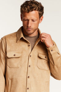 A man wearing a tan suede-like button-up shirt jacket over a taupe sweater, photographed against a clean off-white studio background.
