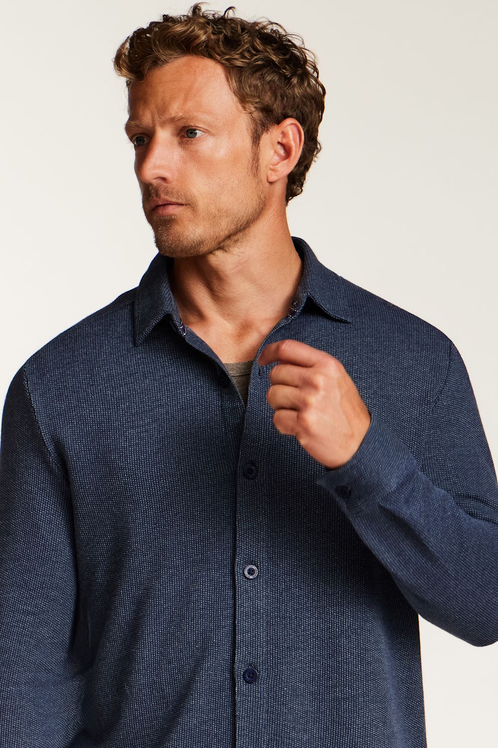 A man wearing a textured navy blue long-sleeve button-up shirt, shown from the chest up against a plain light background.