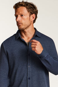 A man wearing a textured navy blue long-sleeve button-up shirt, shown from the chest up against a plain light background.