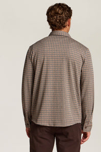 A man viewed from the back wearing a brown and beige checkered long-sleeve shirt and dark brown trousers, set against a plain light gray studio background.