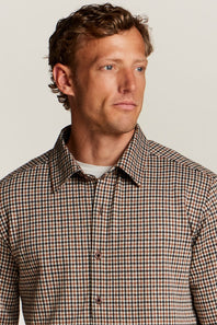 A man wearing a brown and beige checkered button-down shirt, photographed from the chest up against a plain light background.