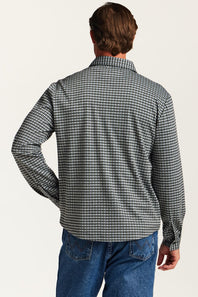A man viewed from behind wearing a long-sleeve button-up shirt with a black and white micro-check pattern, paired with blue jeans, against a plain off-white background.