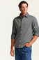 A man wearing a black and white micro-check patterned button-down shirt with rolled-up sleeves, paired with blue jeans, against a plain off-white background.