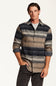 A man wearing a long-sleeve button-up shirt with horizontal stripes in navy, beige, and gray, layered over a light gray t-shirt and dark gray pants, against a plain white background.