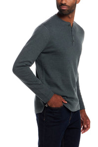 A man wearing a dark gray long-sleeve henley shirt and dark blue jeans, shown from a side profile against a white background.