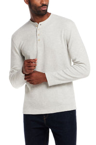 A man wearing a light heather gray long-sleeve henley shirt with three buttons, paired with dark jeans, against a plain white background.