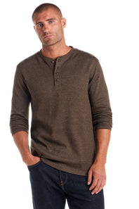 A man wearing a brown long-sleeve henley shirt and dark blue jeans, standing against a plain white background.