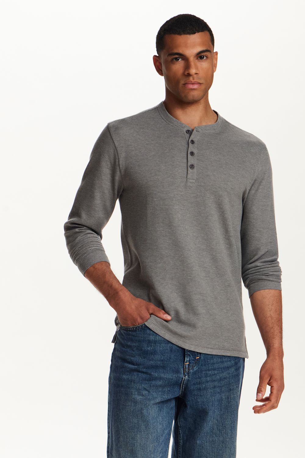 A man wearing a heather gray long-sleeve henley shirt with three buttons on the collar, paired with blue jeans, standing against a plain white studio background.