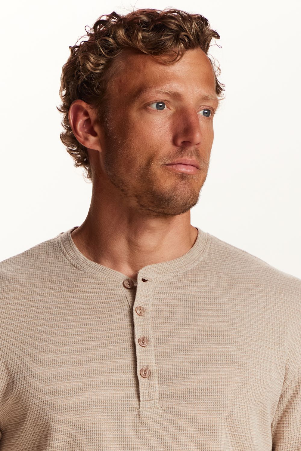 A man wearing a beige waffle-knit henley shirt, shown from the chest up against a clean white background.