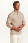 A man wearing a light beige long-sleeve henley shirt and off-white pants, standing against a plain white studio background.