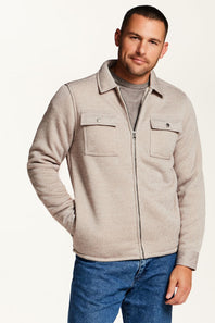 A man wearing a light beige zip-up fleece jacket over a gray t-shirt and blue jeans, photographed against a clean white studio background.