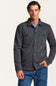 A man wearing a dark gray heathered button-up shirt jacket over a light blue t-shirt and blue jeans, standing against a plain off-white studio background.