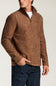 A man wearing a brown textured quarter-zip pullover sweater with a stand collar, paired with dark blue jeans and a white undershirt, shown from the chest down against a light gray studio background.