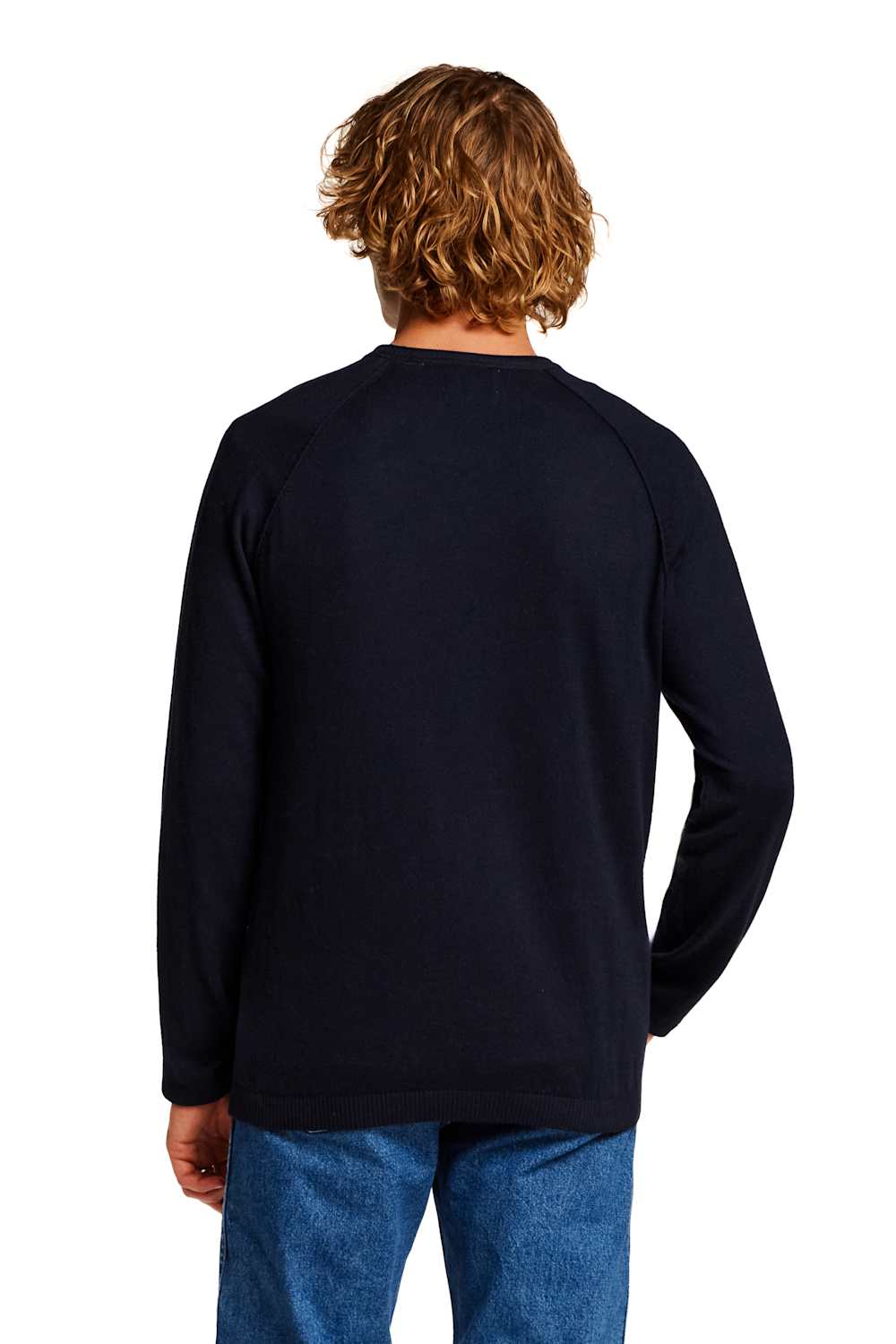 A man with wavy light brown hair is shown from the back wearing a dark navy blue long-sleeve raglan sweatshirt and blue jeans against a plain white background.