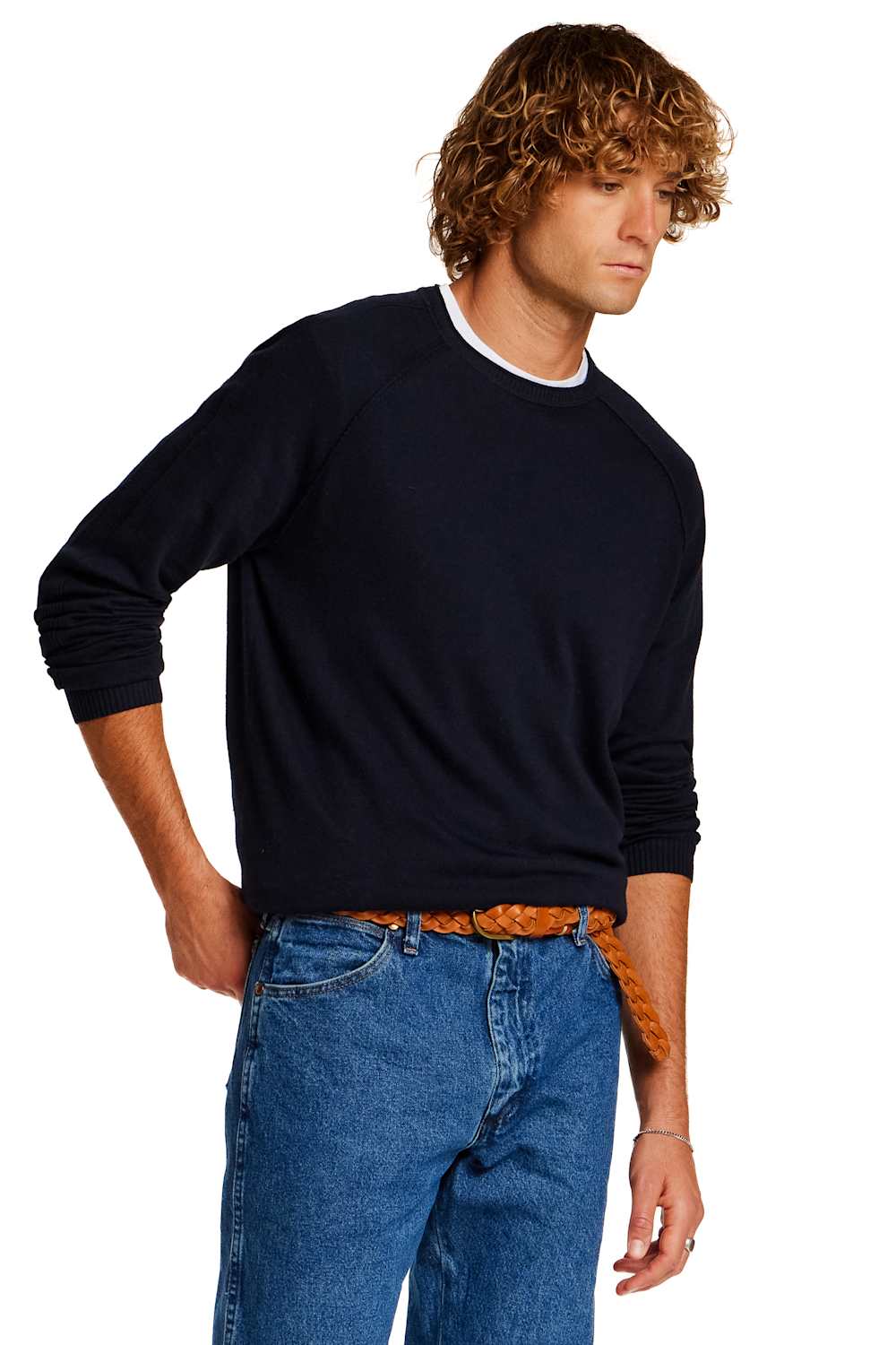 A man wearing a dark navy long-sleeve crewneck sweater with a white ribbed collar, paired with blue jeans and a brown woven belt, photographed against a solid white background.