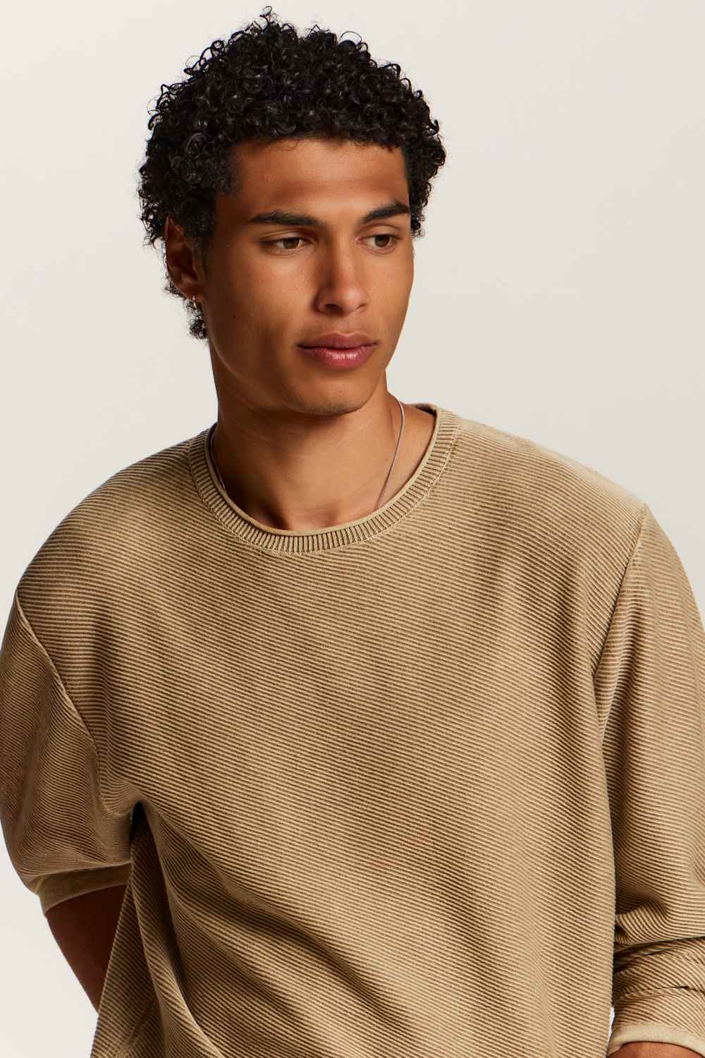 A man wearing a beige ribbed short-sleeve crewneck sweater, photographed against a plain light background.