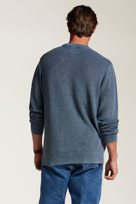 A man viewed from behind wearing a slate blue long-sleeve crewneck sweatshirt and blue jeans against a plain off-white background.