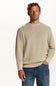 A man wearing a light beige crewneck sweater and blue jeans, standing against a plain white studio background.