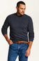 A man wearing a dark heather gray crewneck sweater, blue jeans, and a brown woven belt, photographed against a plain off-white studio background.