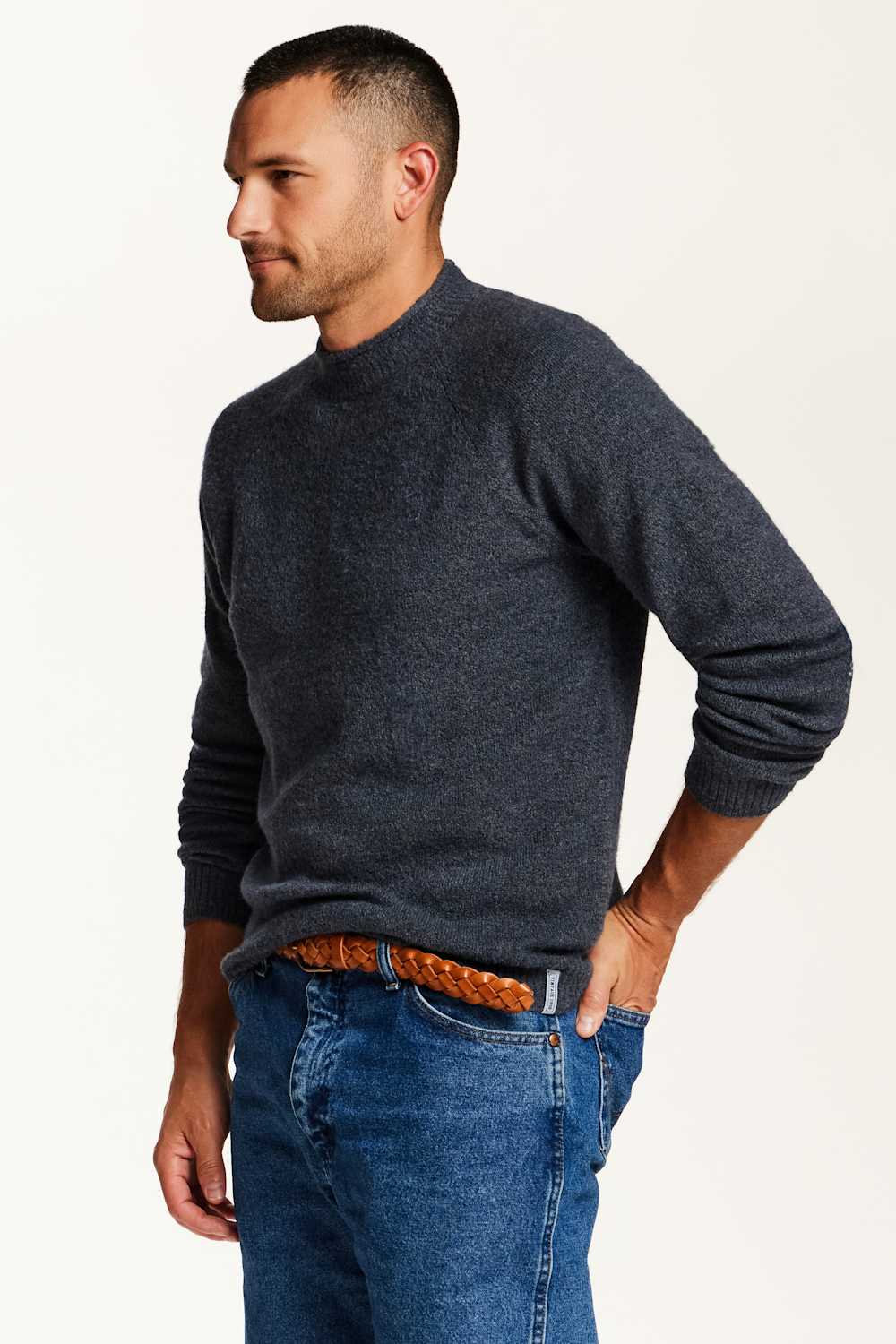 A man wearing a dark charcoal gray knit sweater and blue jeans, shown from the waist up against a plain light background.