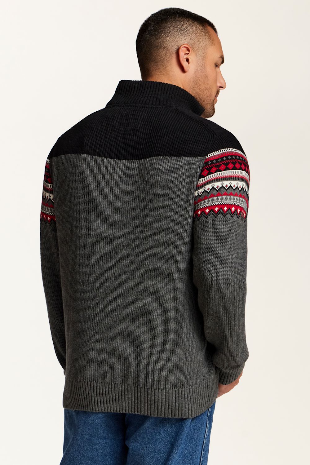 A man wearing a dark gray and black color-blocked knit sweater with red, white, and black Fair Isle patterned yoke and sleeve details, shown from a rear three-quarter view.
