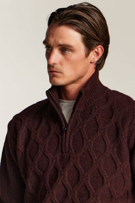A man wearing a dark maroon cable-knit quarter-zip sweater over a light gray t-shirt, photographed against a plain light beige background.