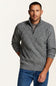 A man wearing a gray cable-knit quarter-zip sweater over a dark gray t-shirt and blue jeans, standing against a plain off-white background.