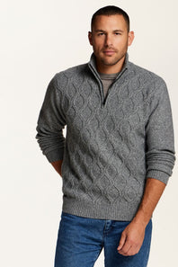 A man wearing a gray cable-knit quarter-zip sweater over a dark gray t-shirt and blue jeans, standing against a plain off-white background.