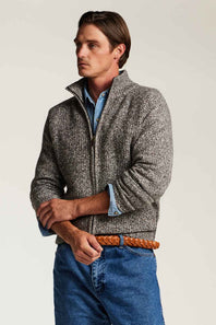 A man wearing a textured gray zip-up jacket over a light blue shirt, paired with blue jeans and a brown braided belt, photographed against a plain light gray studio background.