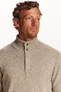 A man wearing a textured, heathered oatmeal-beige knit sweater with a mock neck and a three-button placket, photographed against a clean white background.