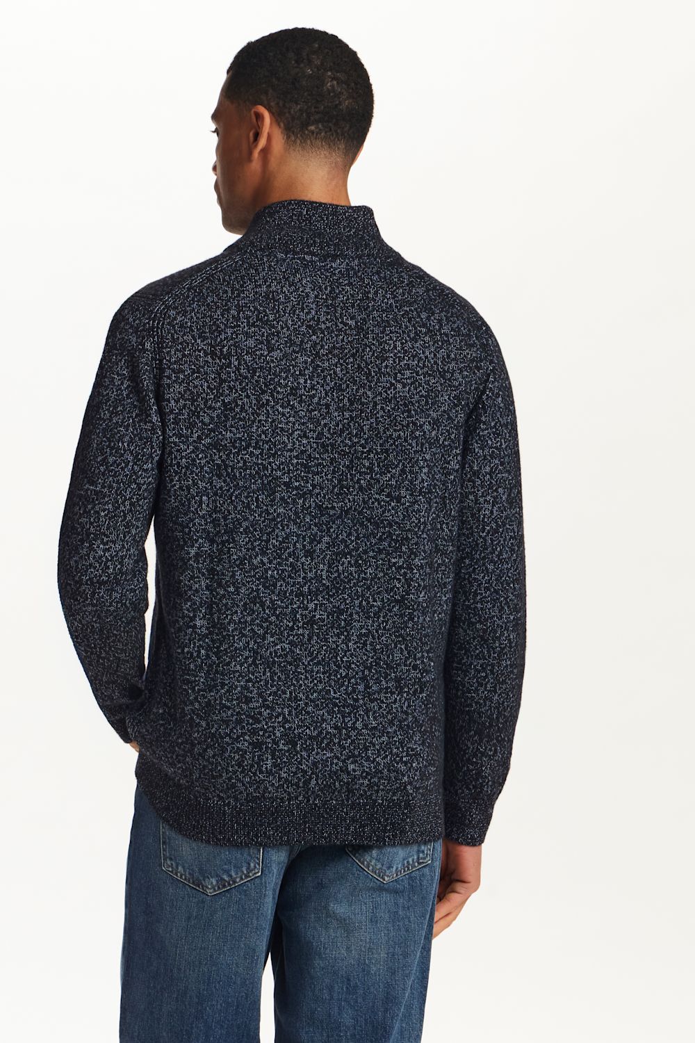 A man viewed from the back wearing a dark navy and black marled knit sweater with blue jeans, set against a plain white studio background.