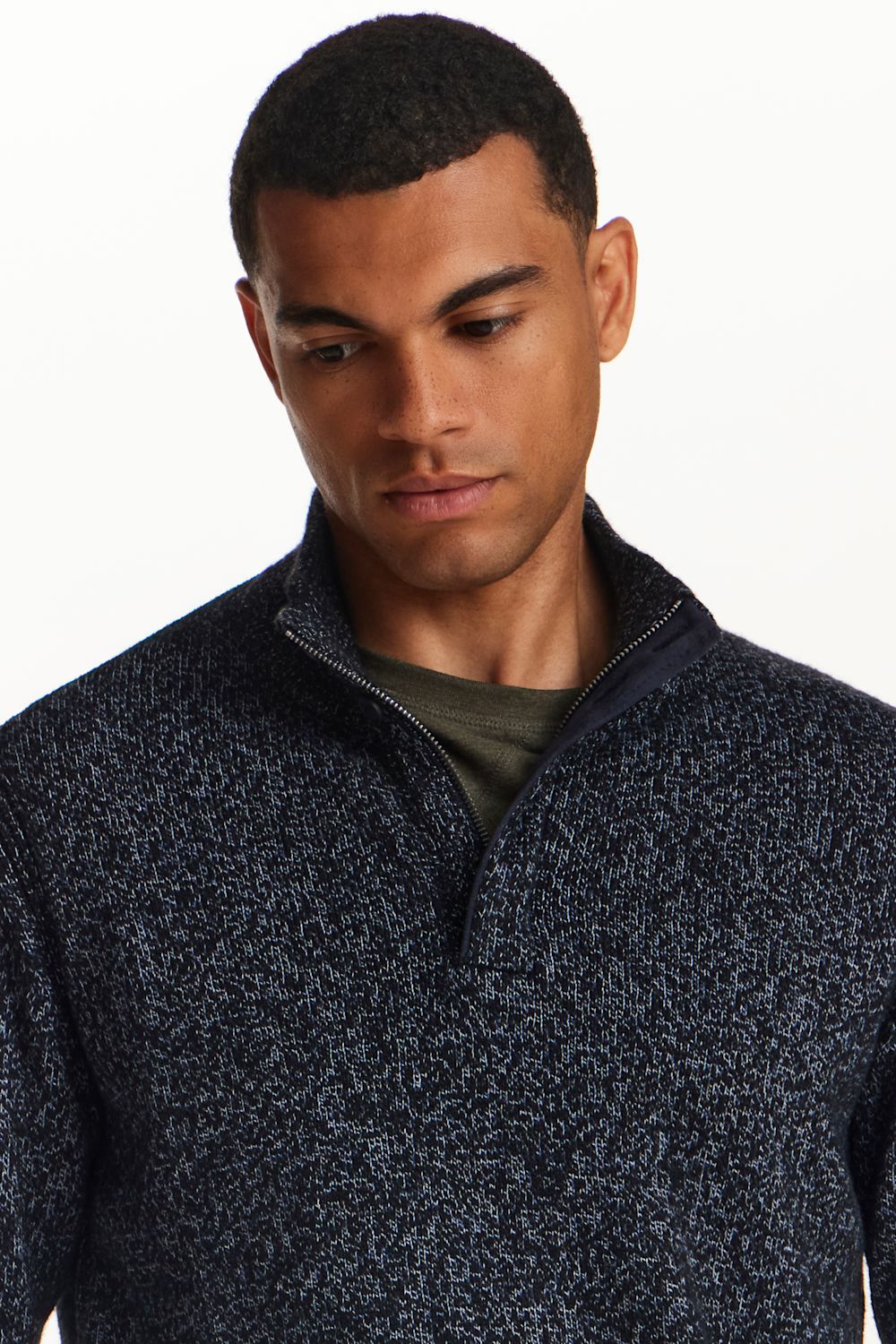 A man wearing a dark navy and black heathered quarter-zip sweater over a dark olive green t-shirt, shown from the chest up against a plain white background.