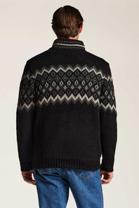 A man viewed from the back wearing a black knit sweater with a cream and gray geometric Fair Isle pattern across the shoulders and upper back, paired with blue jeans against a plain light background.