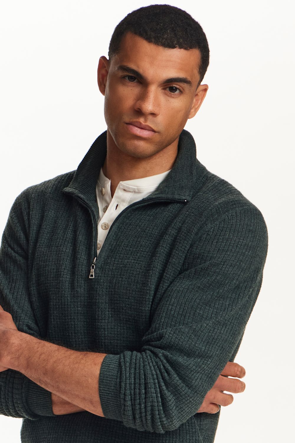 A man wearing a dark green textured quarter-zip sweater over a white collared shirt, photographed against a plain white studio background.
