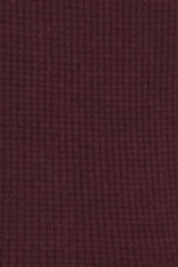 A close-up of a textured fabric swatch in a deep burgundy or maroon color, showing a fine waffle or grid-like weave pattern.