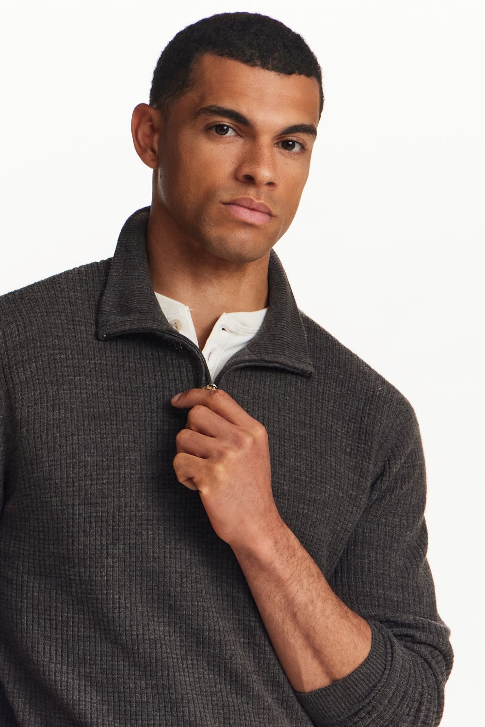 A man wearing a dark gray ribbed quarter-zip pullover sweater over a white collared shirt, shown from the chest up against a plain white background.
