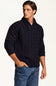 A man wearing a dark navy blue cable-knit sweater with a shawl collar and buttoned placket, paired with blue jeans, photographed against a plain white studio background.