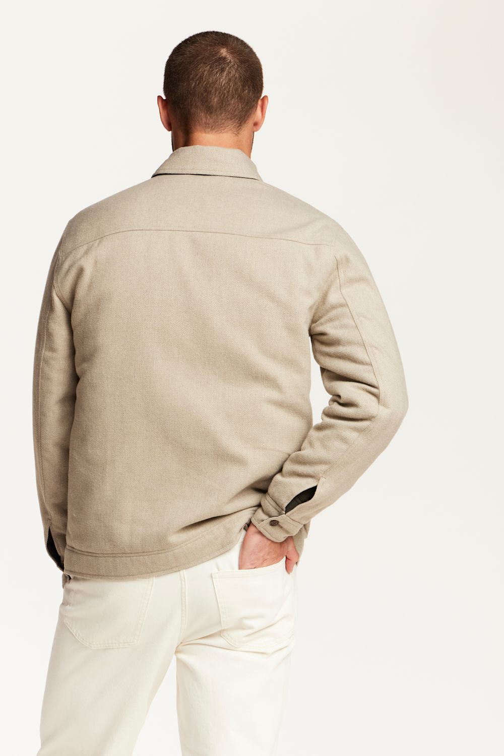 A man shown from the back wearing a light beige jacket and off-white trousers, photographed against a clean white studio background.