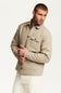 A man wearing a light beige button-up jacket with a chest pocket, paired with off-white trousers, photographed against a clean white studio background.