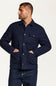 A man wearing a navy blue button-up overshirt jacket with front pockets, paired with dark blue jeans, photographed against a clean off-white studio background.