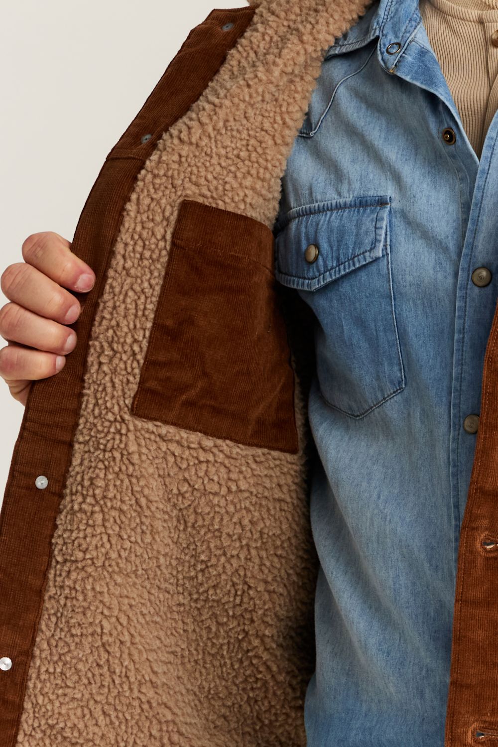 Close-up of a brown suede jacket with a tan sherpa lining, worn over a blue denim shirt.