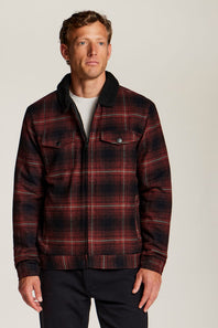 A man wearing a red and black plaid zip-up jacket with a dark corduroy collar, photographed against a plain light gray studio background.